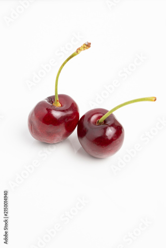 Pair of ripe cherries with glossy skin and green stems on white background, minimalist fruit photography highlighting color and texture