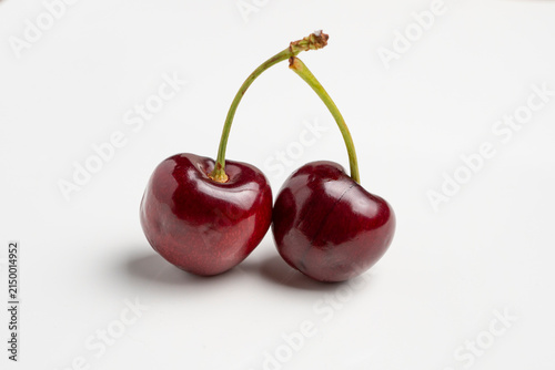 Pair of ripe cherries with glossy skin and green stems on white background, minimalist fruit photography highlighting color and texture