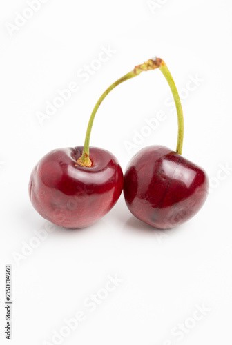 Pair of ripe cherries with glossy skin and green stems on white background, minimalist fruit photography highlighting color and texture