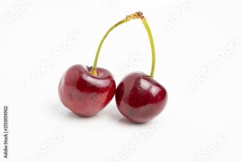 Pair of ripe cherries with glossy skin and green stems on white background, minimalist fruit photography highlighting color and texture