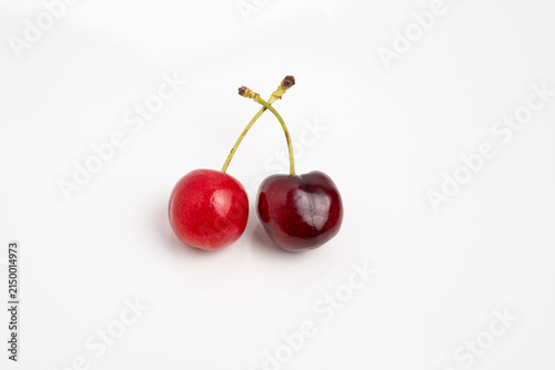 Pair of ripe cherries with glossy skin and green stems on white background, minimalist fruit photography highlighting color and texture