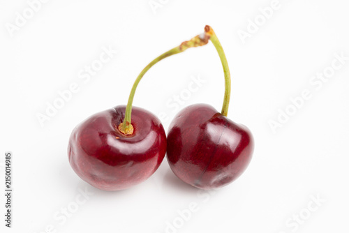 Pair of ripe cherries with glossy skin and green stems on white background, minimalist fruit photography highlighting color and texture