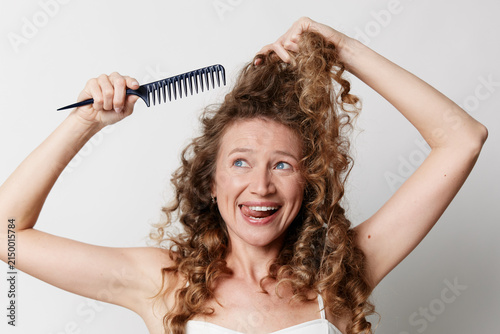 Konstfotografi Mature woman with natural skin and curly hair reacts with surprised expression while brushing hair in a studio setting, candid beauty concept