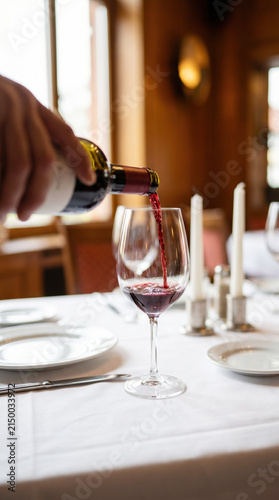 Close up hand of waiter pouring red wine in wine glass on the dining table in restaurant