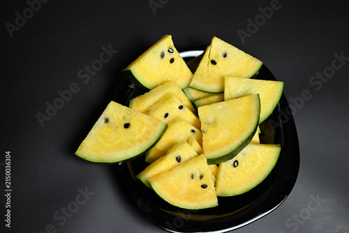 Yellow watermelon cut into triangles on black background