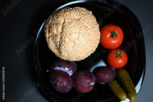 Hamburger with red tomatoes, pickles, and plums on a black background.