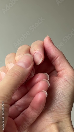 Vertical video close up of female hands applying and rubbing hydrating cosmetic oil into cuticles and healthy natural fingernails. Home beauty routine and skincare concept.