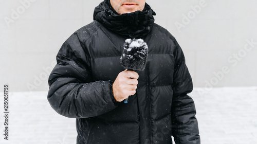 Male journalist reporting in winter snowstorm. Reporter holding microphone covered in snow. Breaking news and live weather coverage