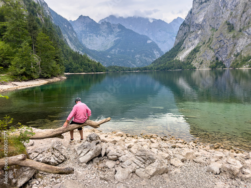 Elderly Man Taking a Break On an old old tree branch in the Bavarian Alps with mountain lake	

