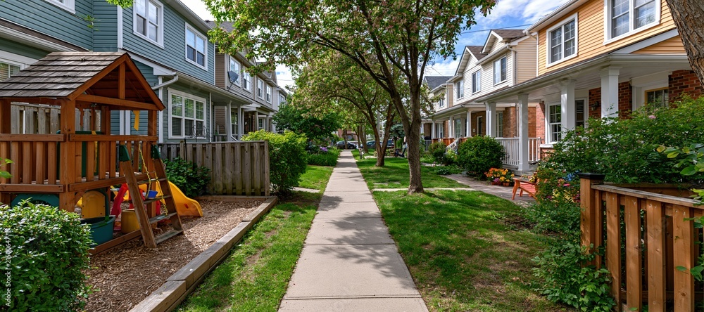 Fototapeta premium Backyard sidewalk with toddler play area and row of family homes in summer