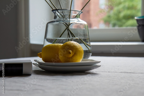 Two lemons on plate near vase and sunlit window
