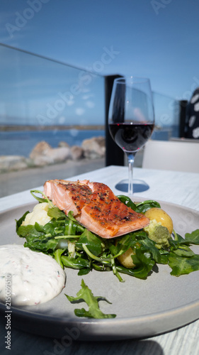 Grilled salmon fillet with salad and red wine by the sea