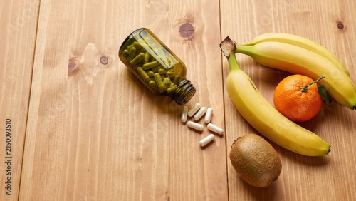 Healthy fruits and daily vitamin supplements for nutritional support on wooden table with vitamins, supplements