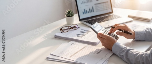 Businessperson analyzing financial documents with laptop and calculator in bright office environment with well lit office desk laptop with professional using calculator