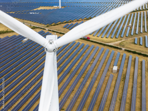 Wind Turbine Blades Looming Over a Vast Landscape Filled With Rows of Solar Panels