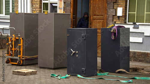 Workers transport large safes outside a building in a busy urban area during daytime hours