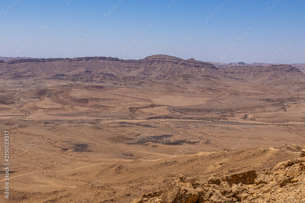 Obraz premium Wide view of the Negev Desert landscape with rugged mountain plateaus, dry valleys and rocky terrain under a clear blue sky.