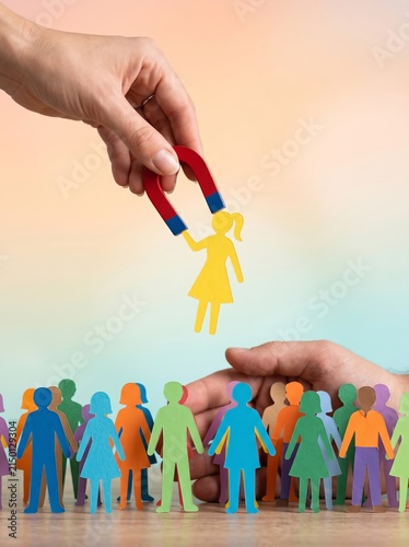 A hand gripping a magnet drawing a paper cutout of a woman amidst vibrant shapes and colors
