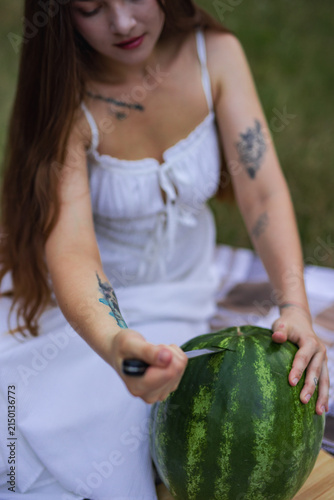 Young woman looking down while cutting watermelon on picnic blanket