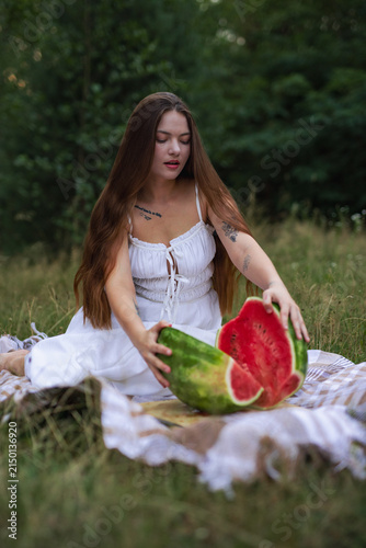 Young woman opening two halves of fresh cut watermelon on picnic blanket