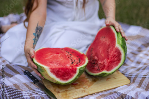 Close up of young woman holding two halves of ripe red watermelon on picnic