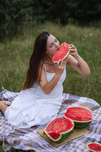 Young woman sitting on picnic blanket and eating slice of ripe watermelon