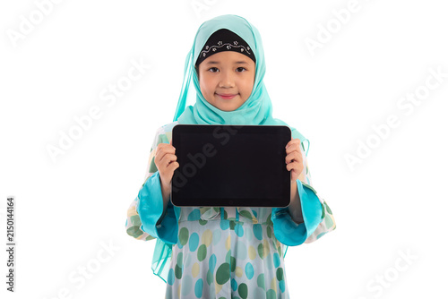 Adorable Muslim girl in mint green hijab showing empty tablet screen mockup smiling at camera in white studio.