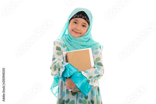Adorable Muslim girl in mint green hijab holding books smiling at camera isolated in white studio.
