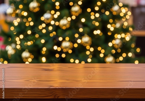 A clean empty brown wooden table stands in front of a festive decorated holiday tree with glowing warm lights and soft bokeh background, showcase, brown, warm