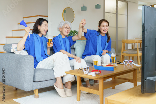 リビングのソファに並んで座ってテレビでサッカー日本代表を応援するミドル世代の日本人女性3人