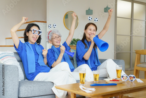 リビングのソファに並んで座ってテレビでサッカー日本代表を応援するミドル世代の日本人女性3人