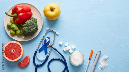 Flat lay composition with healthy food, stethoscope, blue ribbon symbol, and diabetes care supplies on a blue background.