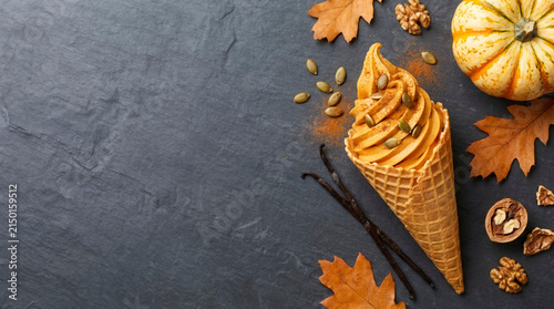 Pumpkin spice ice cream cone with pumpkin seeds and fall leaves on slate, autumn seasonal treat and dessert recipe