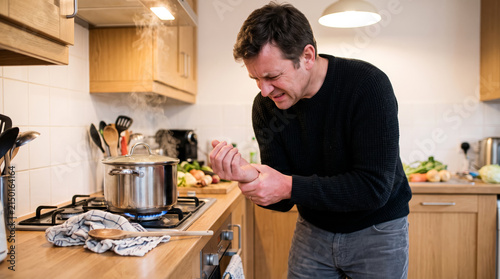 A man holding wrist in pain after touching boiling pot, kitchen accident