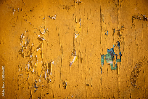 Weathered Yellow Wall with Peeling Paint Layers Revealing Underlying Colors and Old Posters