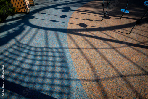 Geometric Shadows of a Children's Playground Climbing Frame Cast on Two-Tone Rubber Safety Flooring at Low Sun Angle