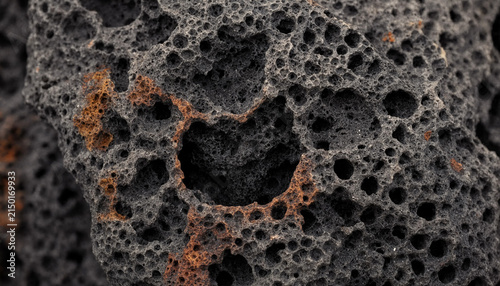 Fotografie Macro detail of a dark volcanic rock featuring a large central hole surrounded b