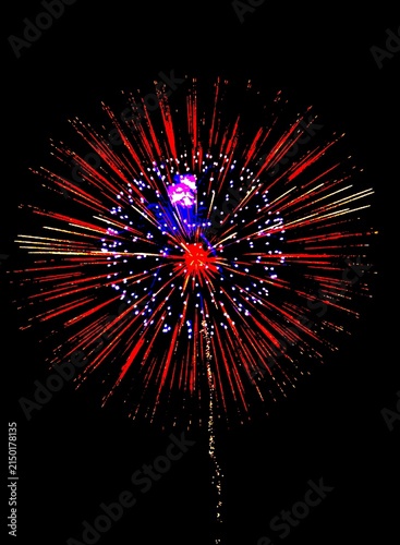 Vibrant red and purple fireworks exploding in the dark night sky. Bright radial light rays and smoke trails against a black background. Perfect for celebration and festive event concepts.