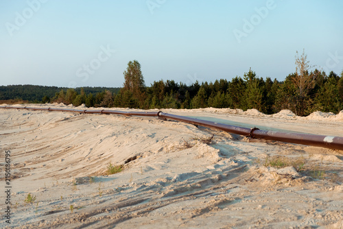 Long industrial pipeline laid across sandy terrain with forest backdrop