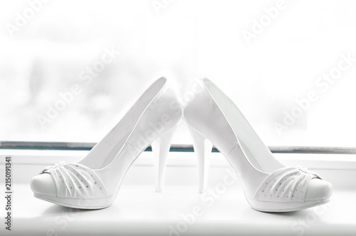 Quadro su tela Elegant white bridal high heels positioned on a windowsill, evoking wedding anticipation, romance, femininity and refined style for bridal fashion, accessories, and ceremony preparations