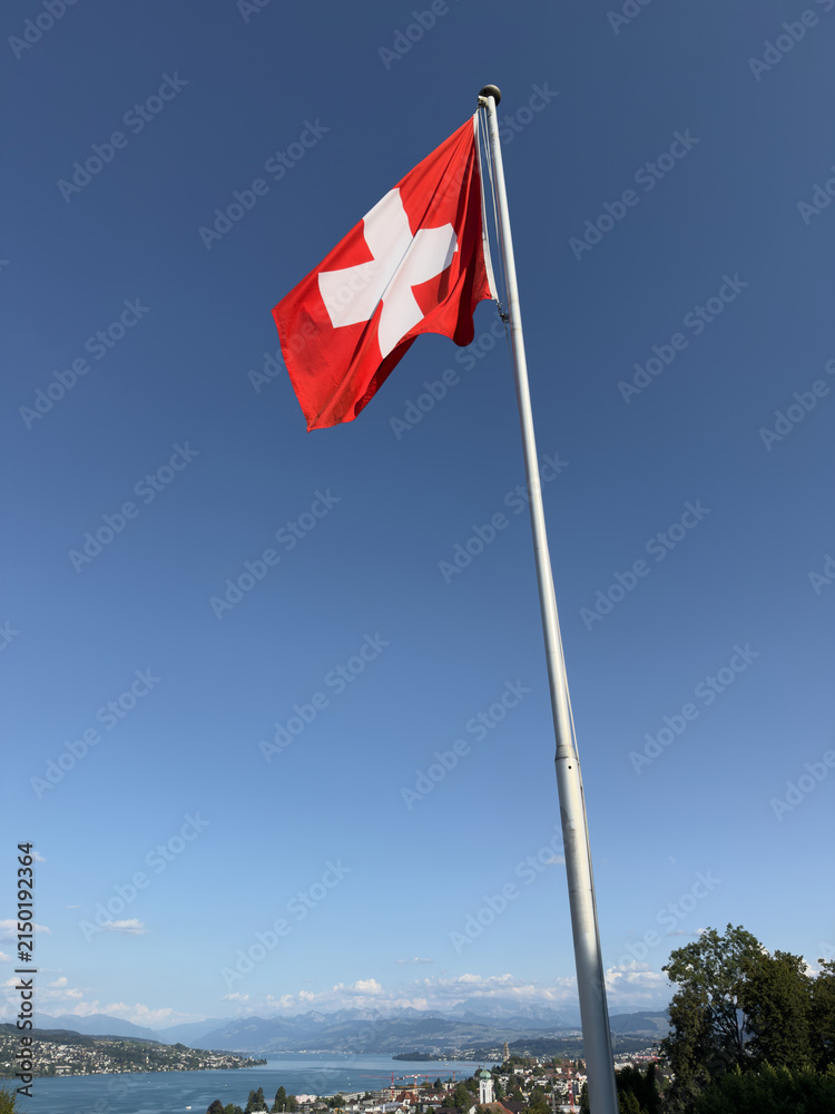 Fototapeta premium Waving Swiss Flag with Lake and Alps in the Background, Switzerland