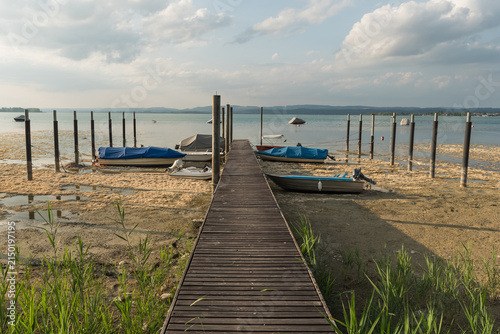 Low water level at Lake Constance: Stranded boats on a dry lake bed next to a wooden jetty during a summer drought in Berlingen, Switzerland.