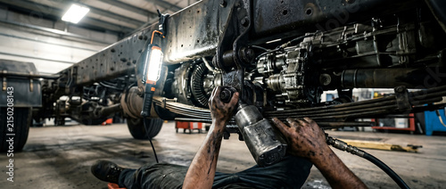 Mechanic repairing heavy truck chassis in workshop