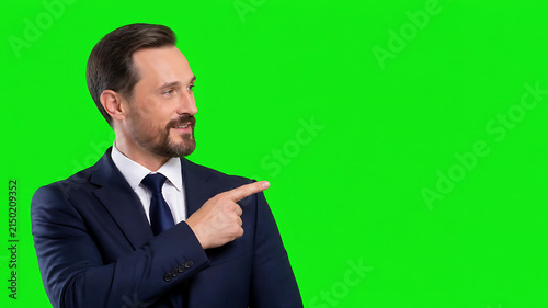 Confident businessman in a suit pointing to the side on a green screen background, isolated for compositing