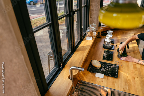 Принти на полотні Modern specialty cafe counter with barista preparing matcha beside large industr