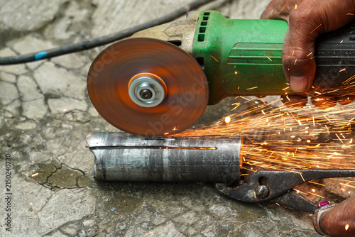 Photography Hand operating angle grinder cutting metal pipe sparks flying concrete ground industrial workshop scene close up action shot tool usage construction repair maintenance task detailed view practical