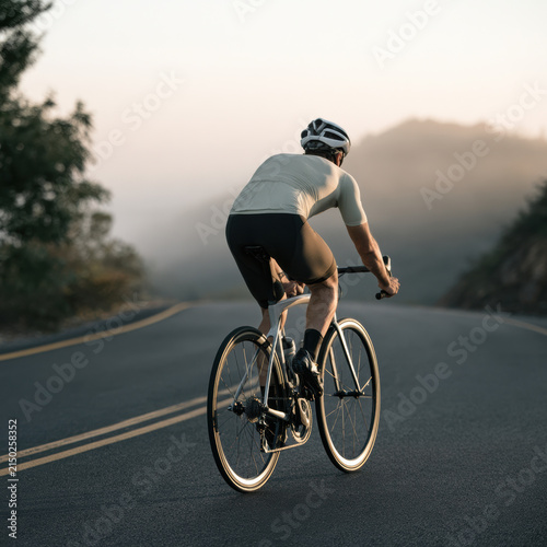 Cyclist road mountain morning helmet athletic outdoor fitness curve sunlight. Cyclist rides winding mountain road sunrise wearing helmet