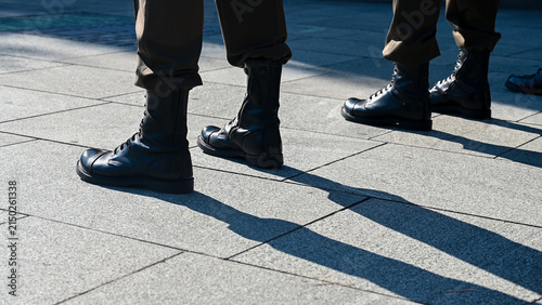 A formation of soldiers wearing camouflage trousers and black combat boots standing in a neat line during a military drill. A row of military personnel dressed in matching tactical camouflage uniform.