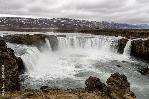 Godafoss waterfall flowing over volcanic basalt cliffs under overcast sky in Northern Iceland