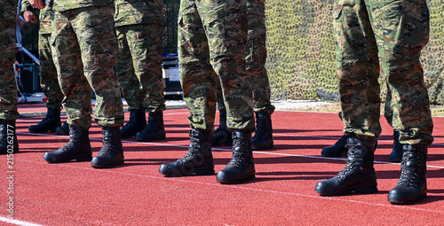 фотографія A formation of soldiers wearing camouflage trousers and black combat boots standing in a neat line during a military drill